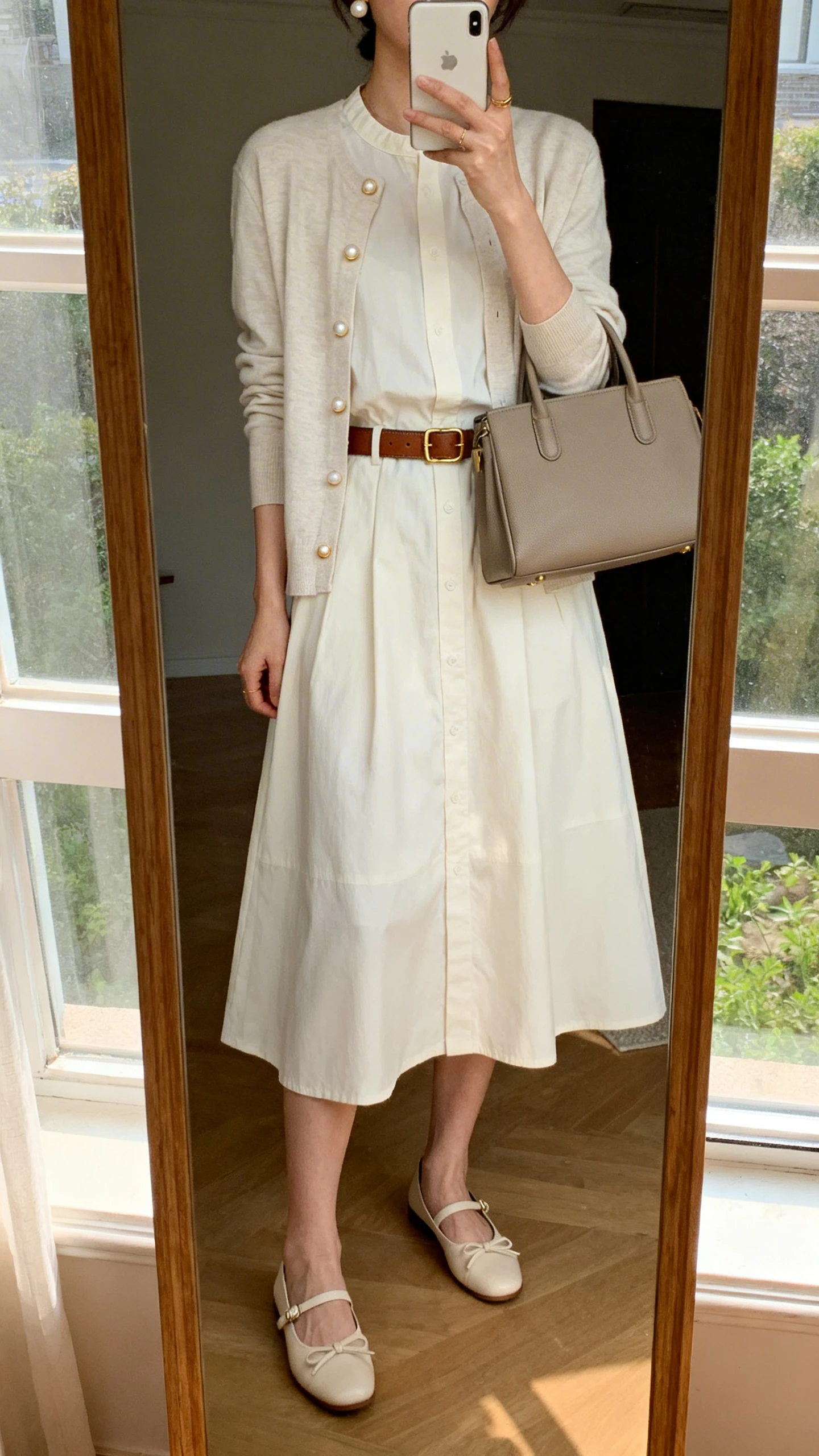 iPhone mirror selfie of a woman in a cotton/poplin day dress (knee to midi) with a lightweight cardigan, classic loafers or ballet flats, pearl or gold studs, a structured tote or satchel, and an optional leather belt, face not visible, cropped at shoulders, full-length mirror by window, natural morning light, iPhone photo quality.
