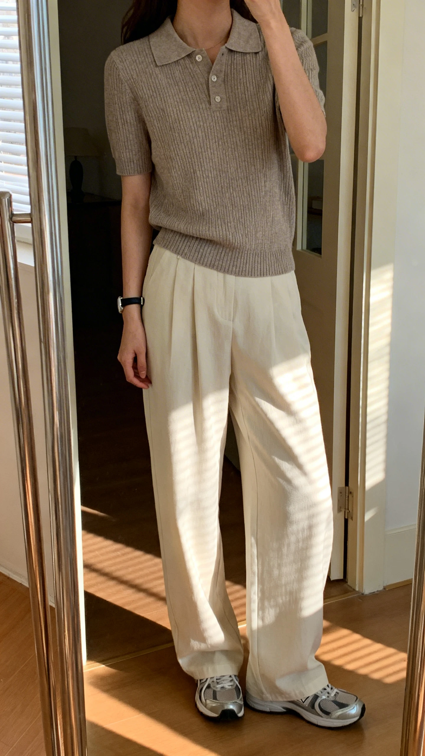 iPhone mirror selfie of a woman in a polo knit top with wide-leg pants and sleek trainers, minimalist watch, face not visible, cropped at neck, entryway full-length mirror, morning light, iPhone photo quality.