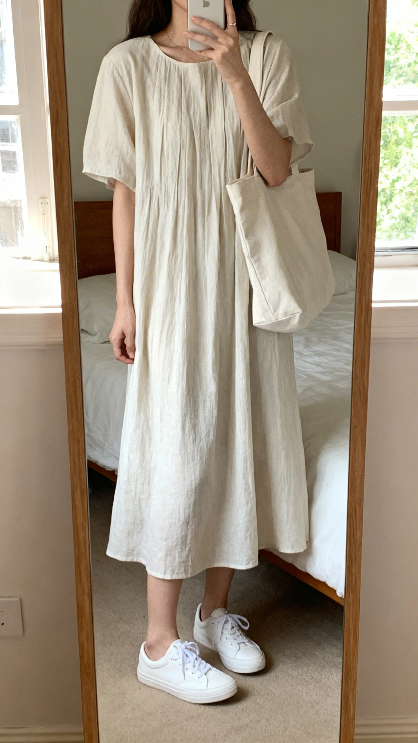 iPhone mirror selfie of a woman wearing a breezy midi dress with crisp white sneakers and a simple tote, face not visible, cropped at neck, bedroom mirror, soft morning window light, iPhone photo quality.