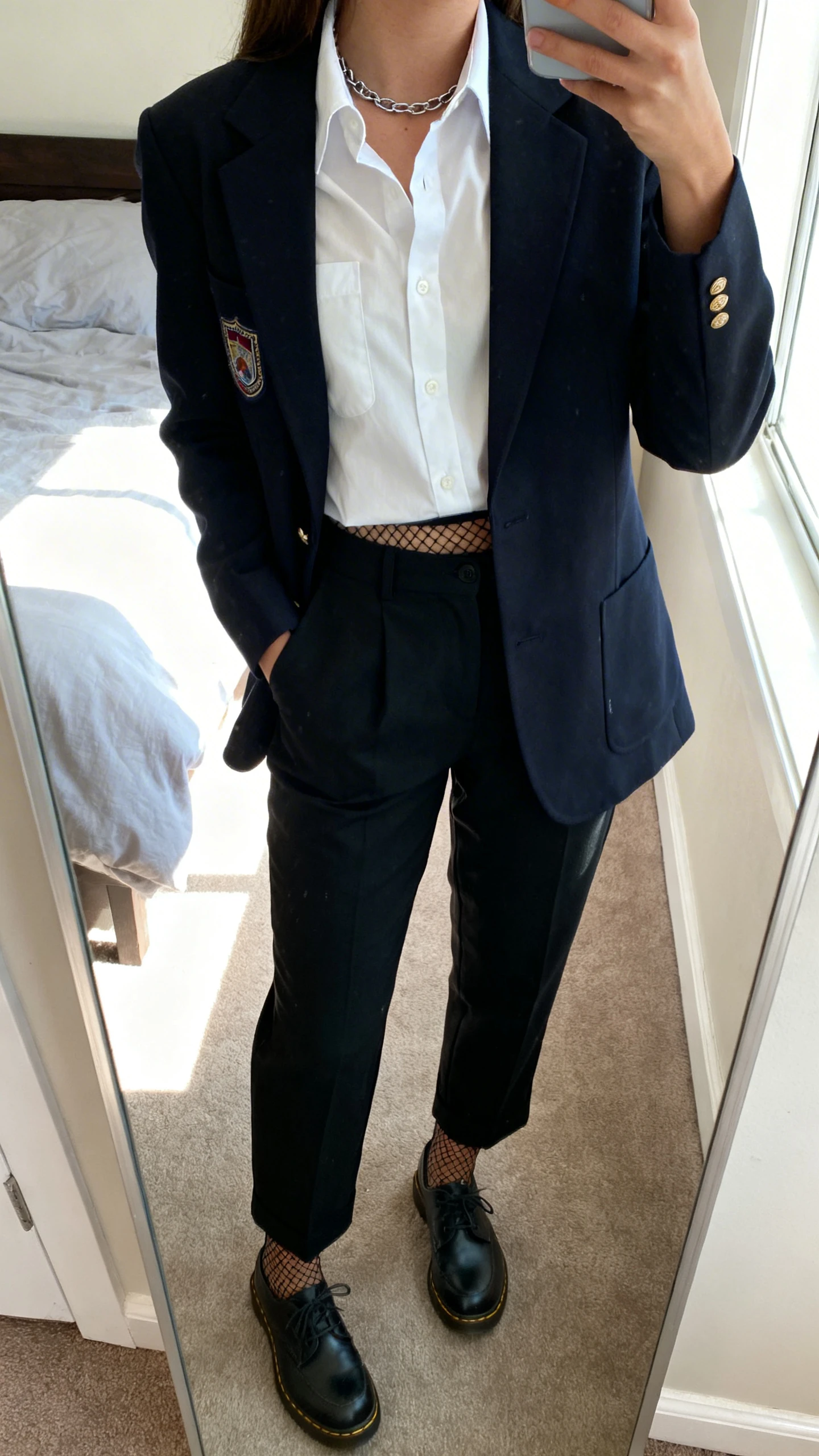 iPhone mirror selfie of a woman wearing a dark academia blazer over a crisp white button-up, black high-waisted trousers, oxford shoes, subtle chain necklace, and a secret-edge detail like a peek of fishnet tights, face not visible, cropped at neck, bedroom mirror, morning window light, iPhone photo quality