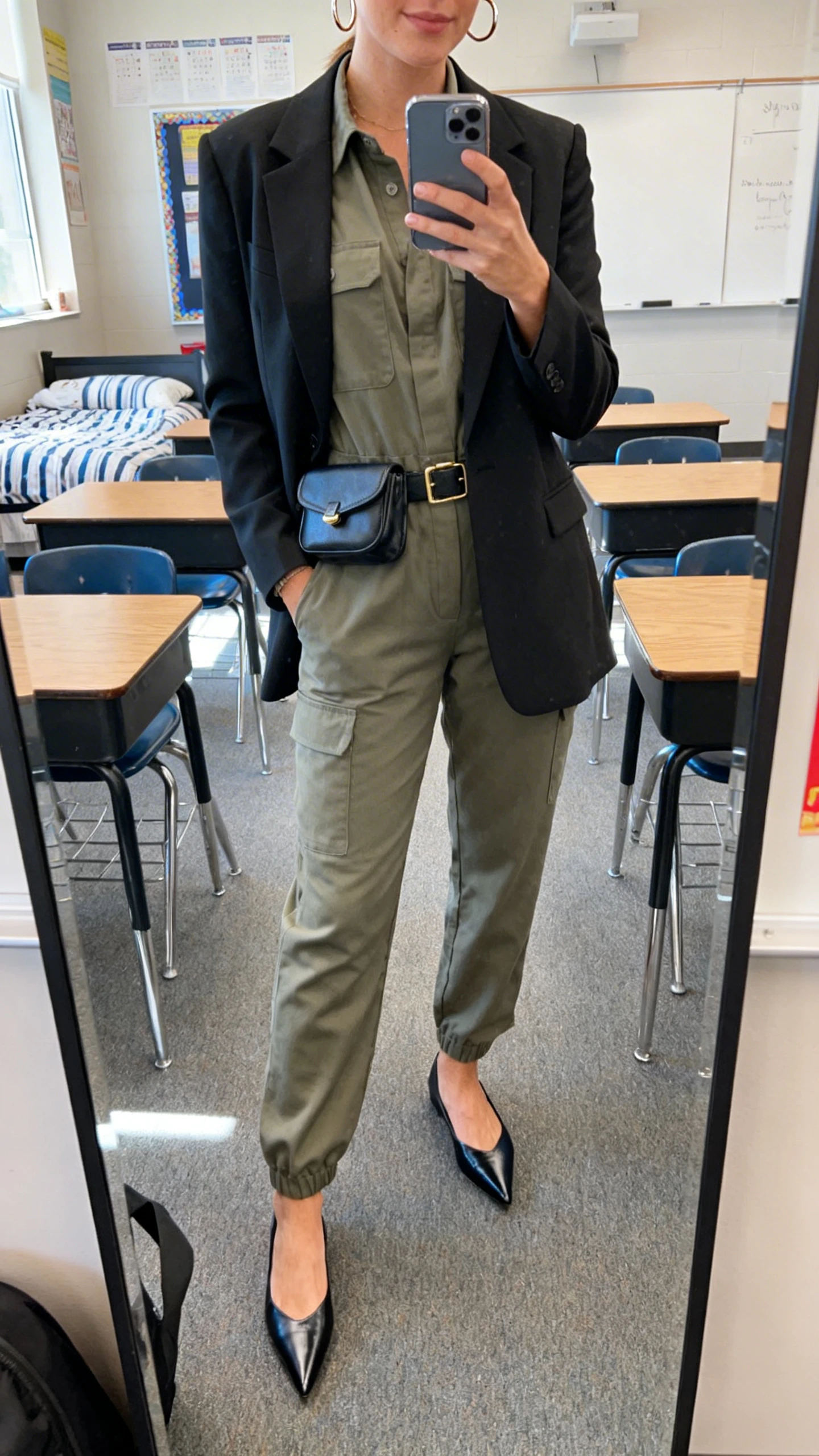 iPhone mirror selfie of a woman wearing a teacher-approved utility jumpsuit layered with a smart blazer, pointed flats, belt bag and simple hoop earrings, face not visible, cropped at shoulders, classroom-like bedroom mirror, natural daylight, iPhone photo quality