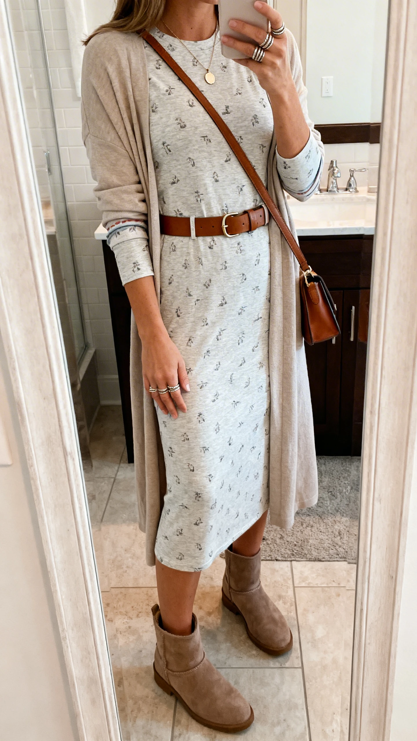iPhone side-angle mirror selfie of a woman in a jersey midi dress with sleeves (subtle print), lightweight longline cardigan, cushioned ankle boots, leather belt, delicate pendant necklace with stackable rings, and a crossbody bag, face not visible, bathroom mirror, soft indoor lighting, iPhone photo quality.