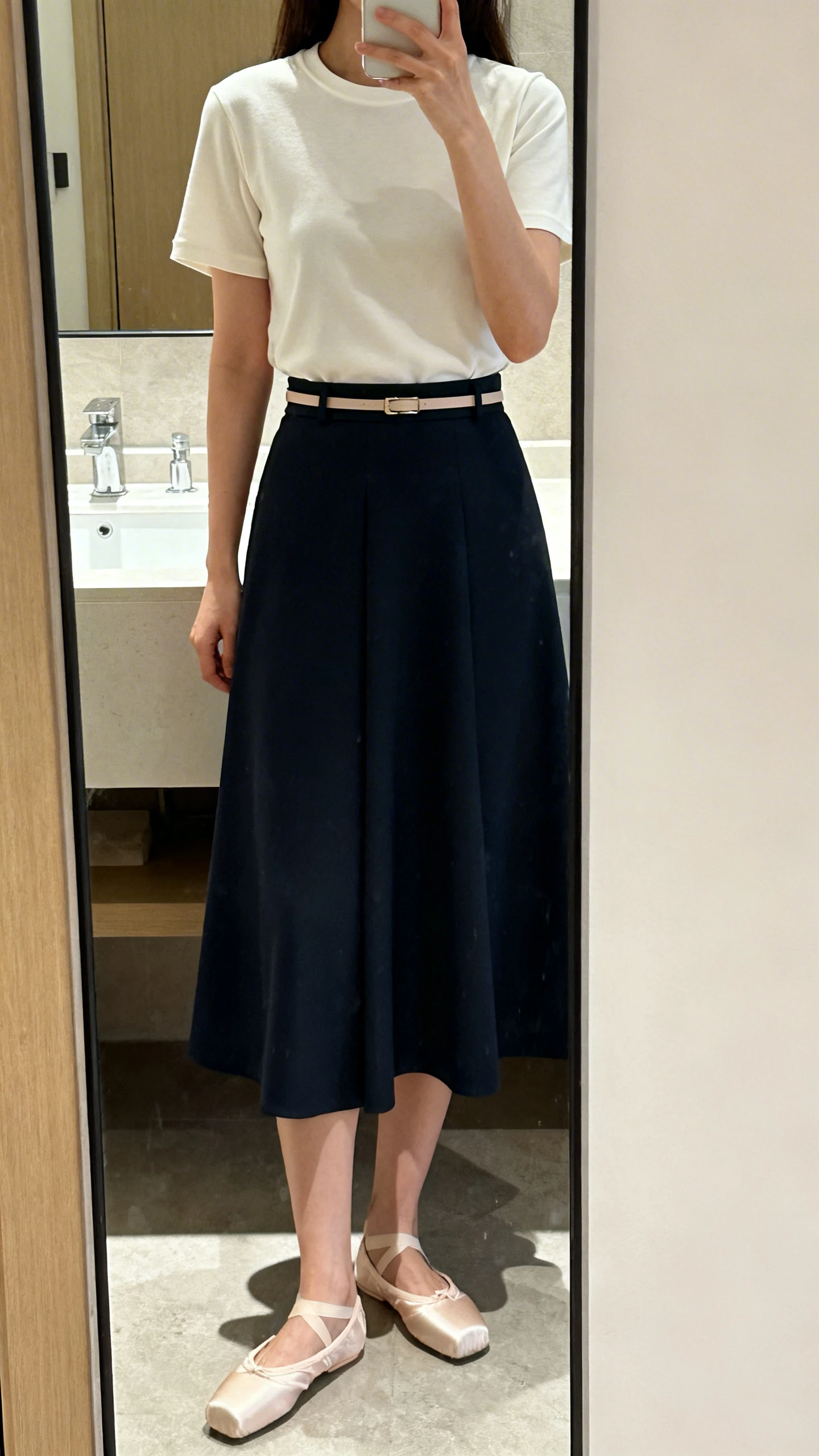 iPhone side mirror selfie of a woman wearing a polished crewneck T-shirt tucked into an A-line skirt, classic ballet flats, and a thin belt, face not visible, bathroom mirror, soft indoor light, iPhone photo quality.
